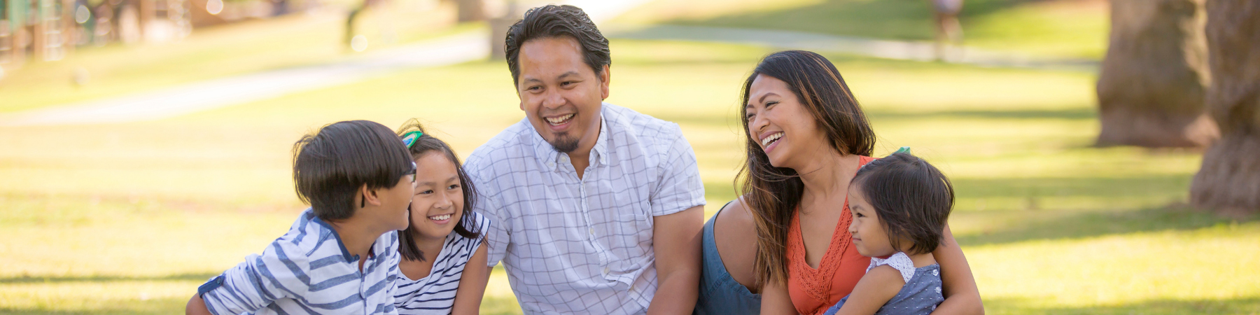Happy Asian American and Pacific Islander family sitting together on the grass 