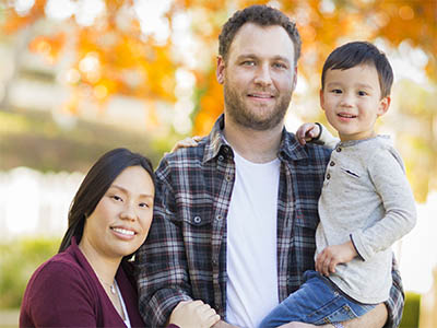 Asian mother and Caucasian father holding son and smiling. Multiracial family outdoors during autumn and fall.